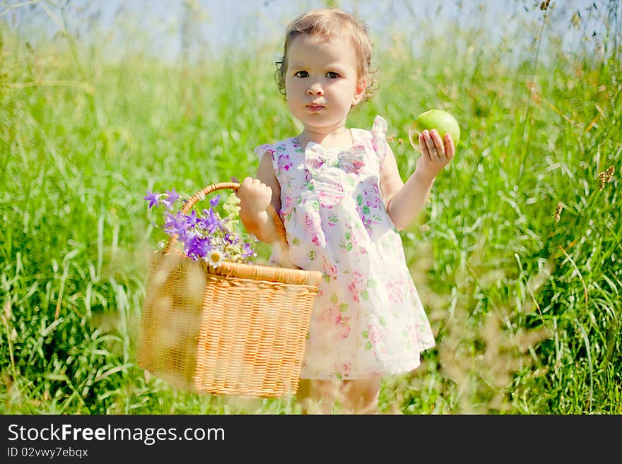 Little beautiful girl holding picnic basket in one hand and green apple in another one. Little beautiful girl holding picnic basket in one hand and green apple in another one