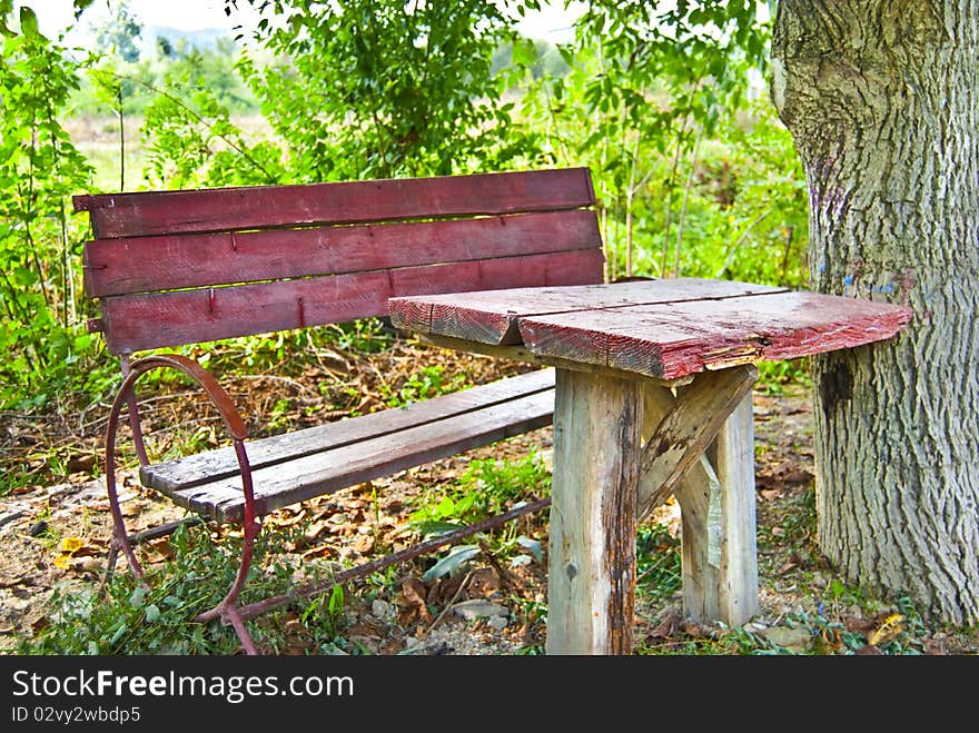 A red table with a chair near a tree