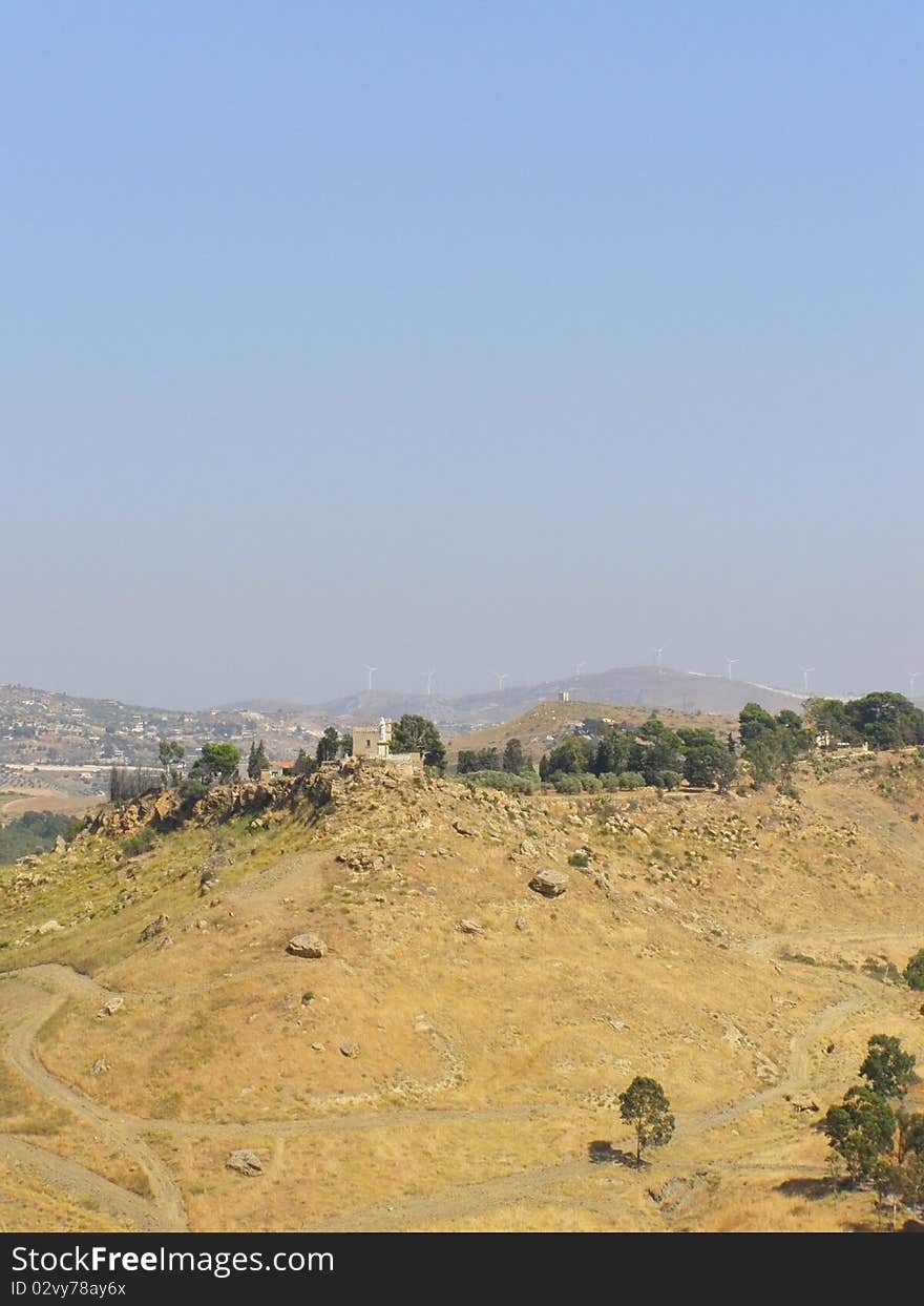 Vertical rural landscape, with house on the hilltop and modern windmills in the background; *with space for text (copyspace)