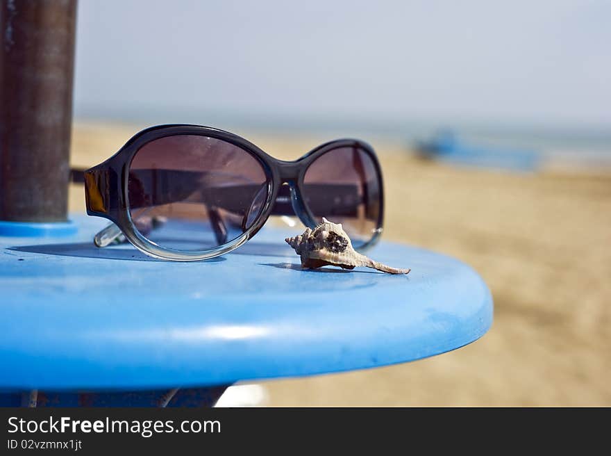 Sun glasses on a beach table and a shell