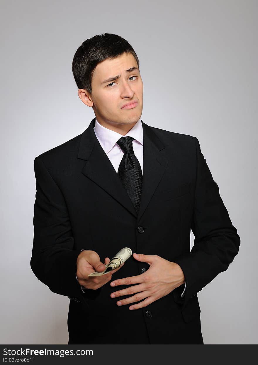 Expressions - Young handsome business man in black suit and tie giving money unhappy. gray background. Expressions - Young handsome business man in black suit and tie giving money unhappy. gray background