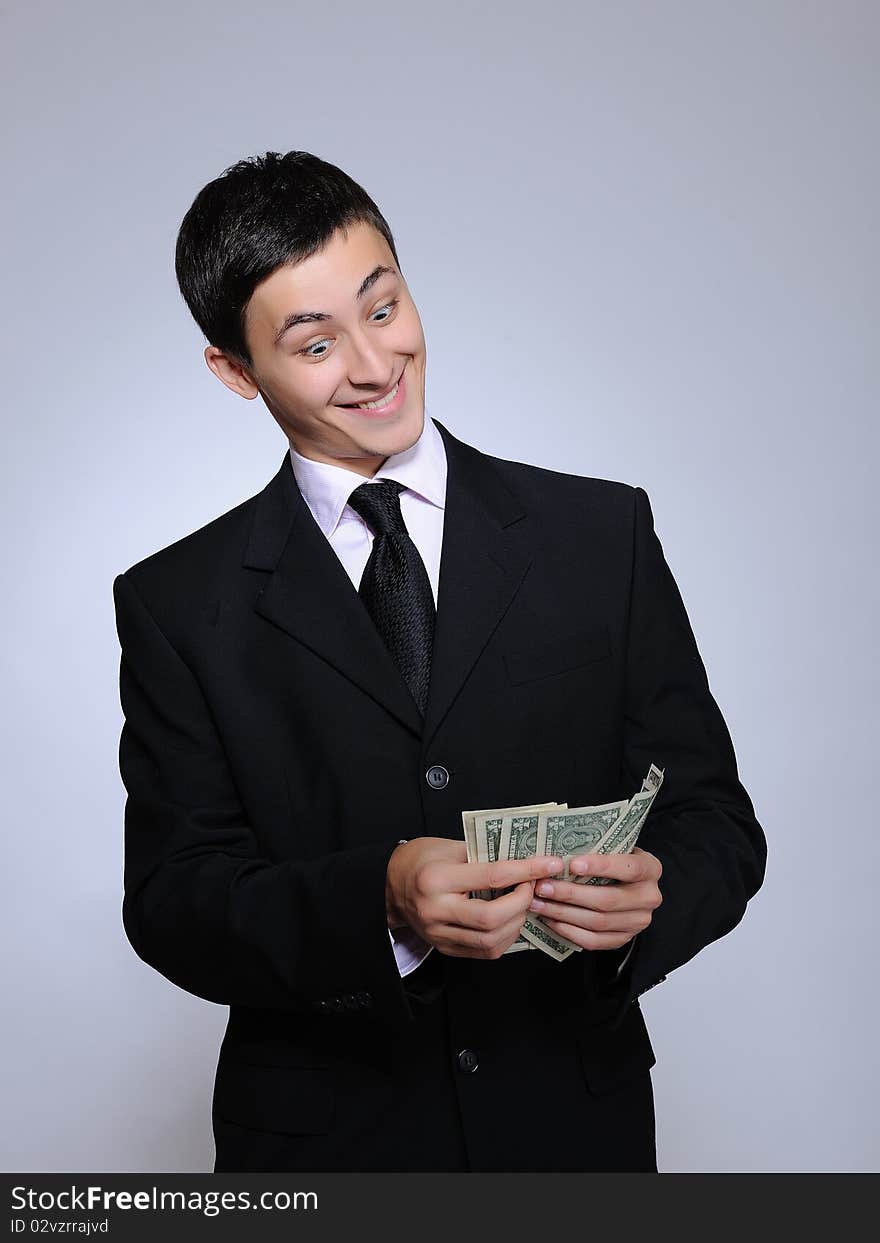 Expressions - Young handsome business man in black suit and tie giving money unhappy. gray background. Expressions - Young handsome business man in black suit and tie giving money unhappy. gray background