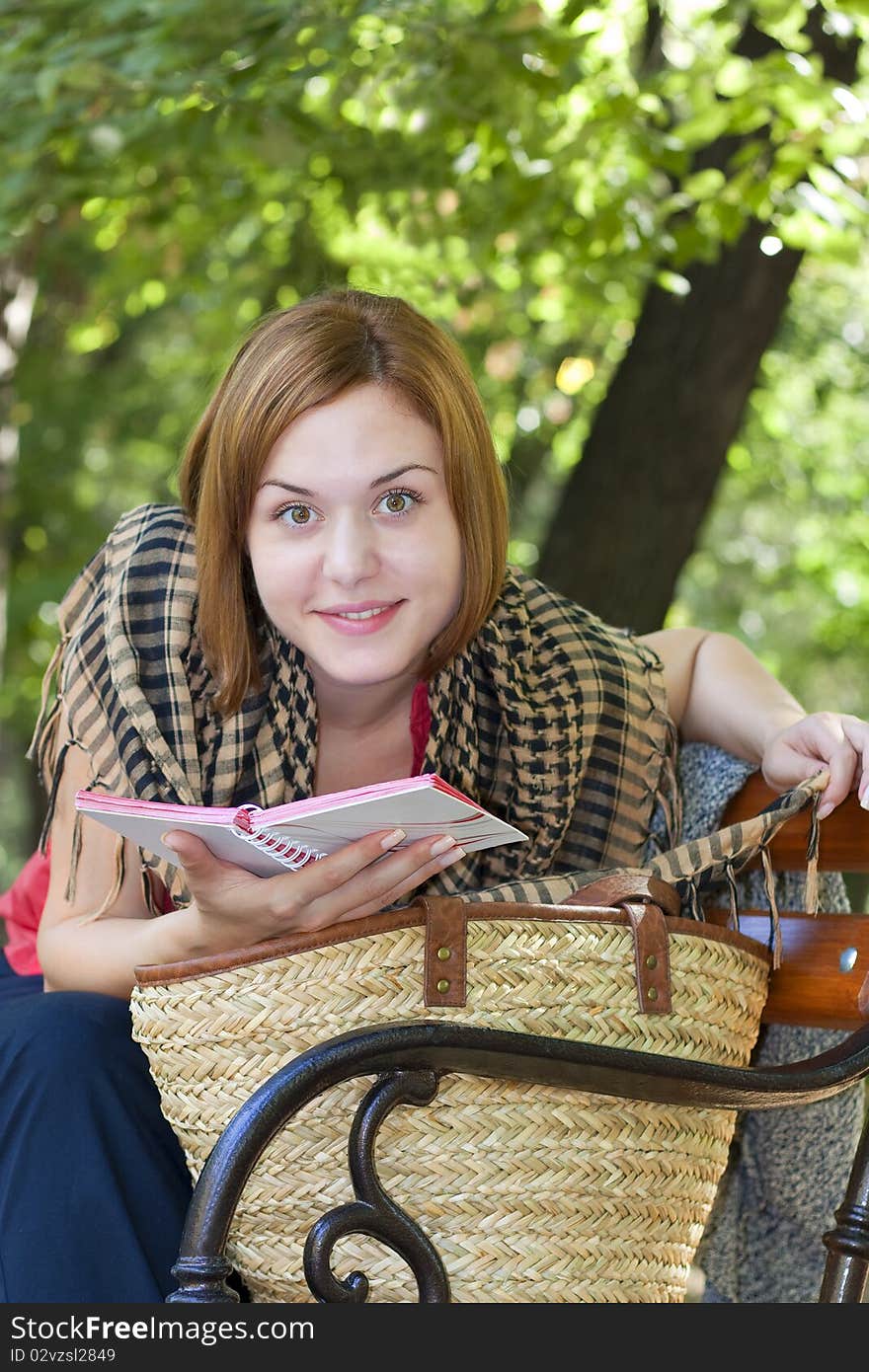 Red-haired woman sitting on a bench with book and smilling at the camera. Red-haired woman sitting on a bench with book and smilling at the camera