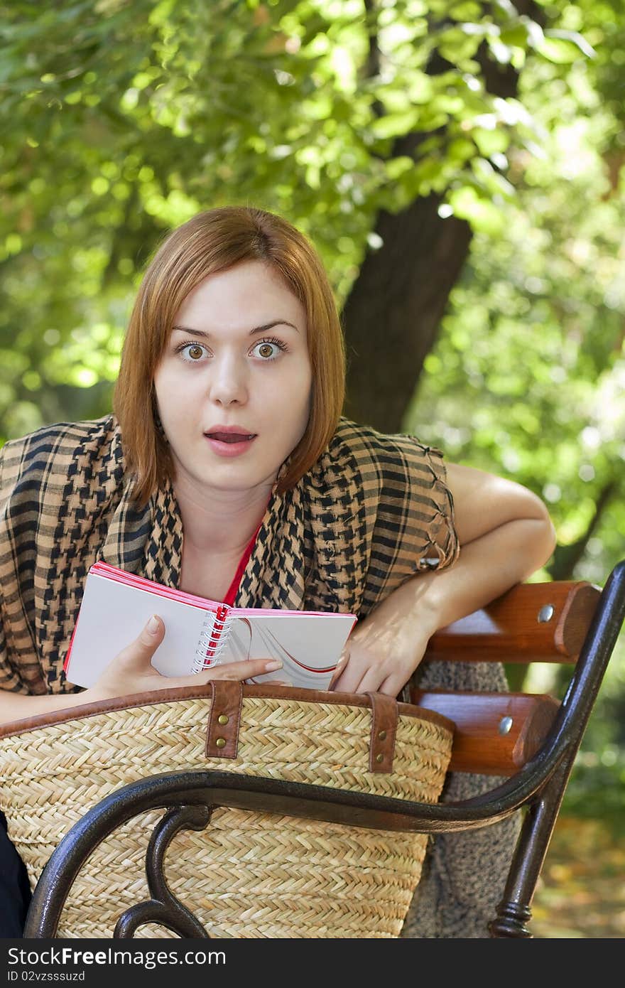 Beautiful red-haired woman reading and looking surprised on a bench