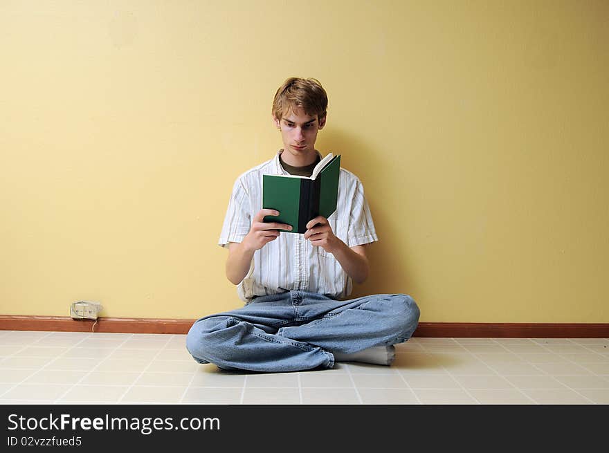 A young male reading a small hardcover book in an empty room with lots of copyspace around his body. A young male reading a small hardcover book in an empty room with lots of copyspace around his body.