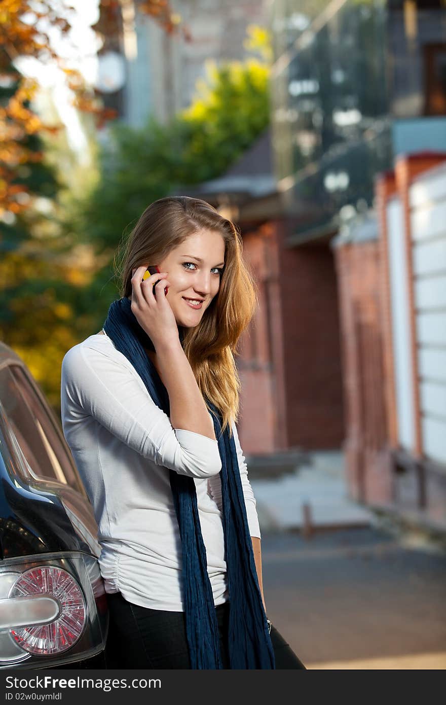 Beautiful blond female on the phone reclined against the car outdoors. Beautiful blond female on the phone reclined against the car outdoors