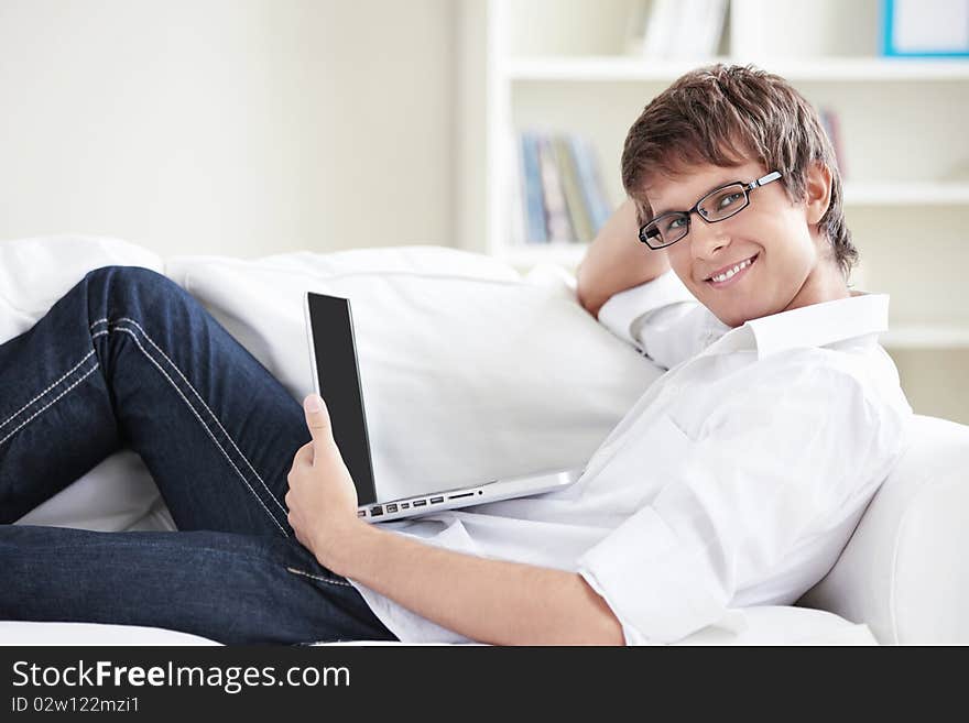 A young man in glasses with a laptop on the couch. A young man in glasses with a laptop on the couch