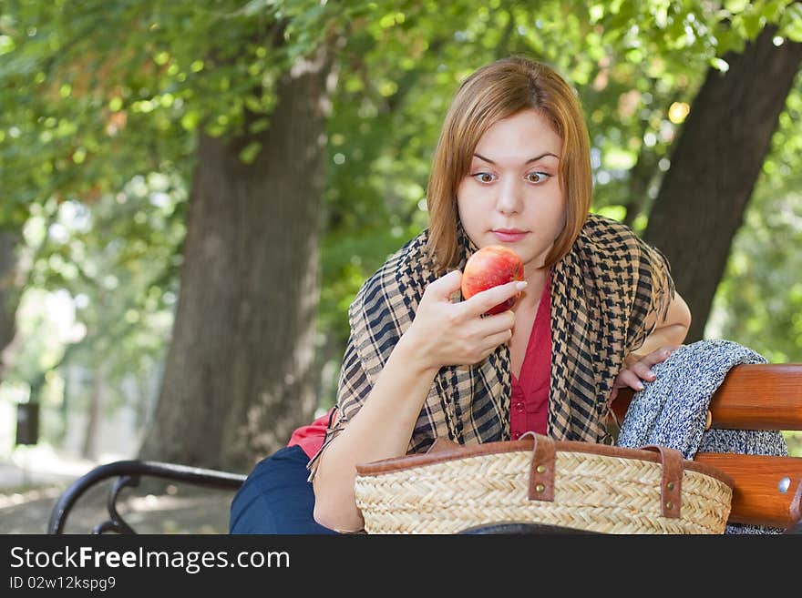 Red-haired woman sitting on a bench and looking at apple. Red-haired woman sitting on a bench and looking at apple