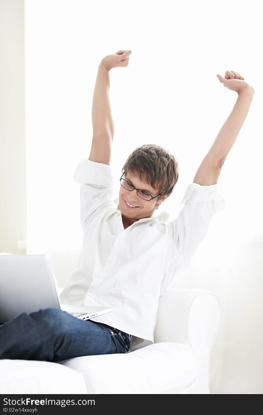 A young man with a laptop at home against the window