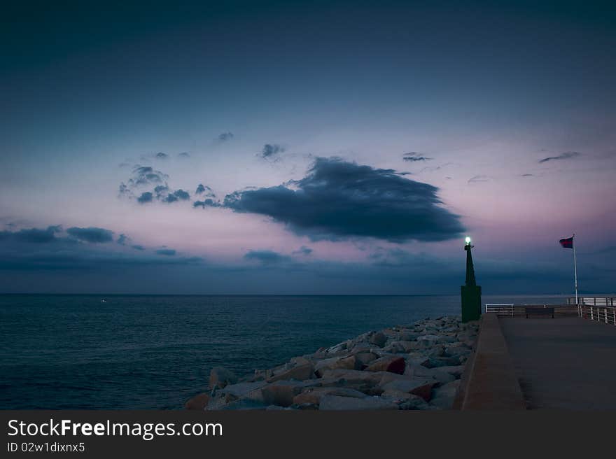 A breakwater at sunrise, with a big dark cloud in the sky and a beacon.