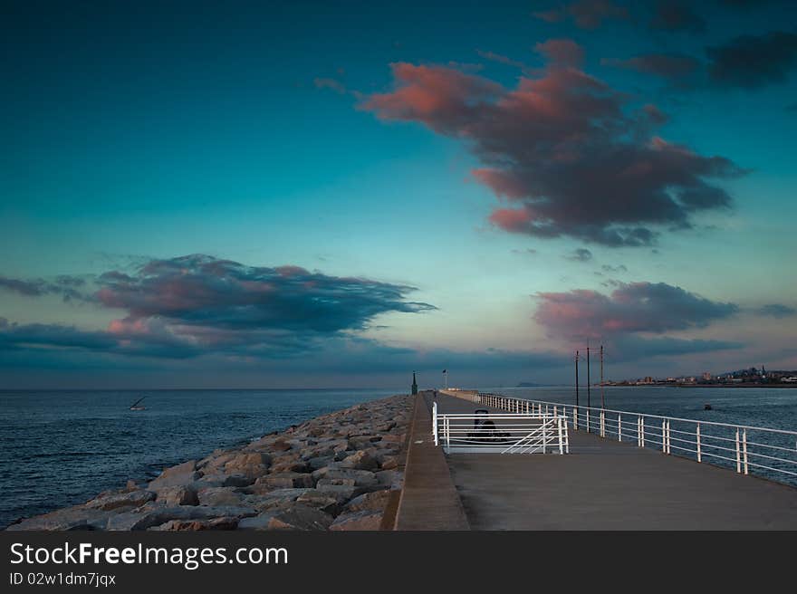 A breakwater at sunrise, with big dark clouds in the sky.