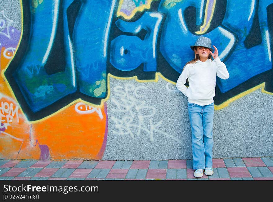 Fashionable stylish beautiful girl standing near a wall with graffiti. Outside. Fashionable stylish beautiful girl standing near a wall with graffiti. Outside