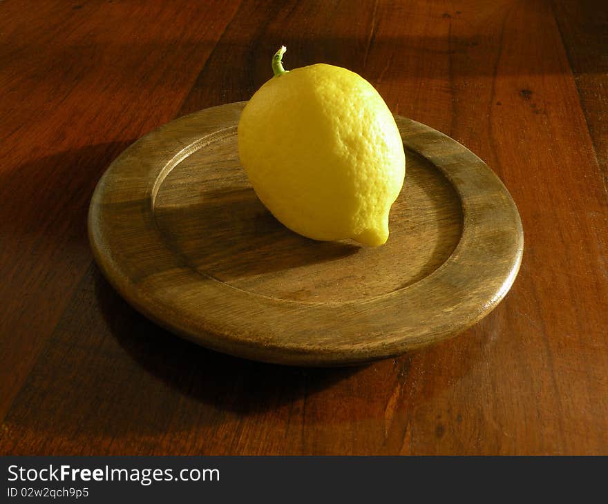 Photograph of a lemon perched on a round plate of wood, which in turn rests on a wooden table. Photograph of a lemon perched on a round plate of wood, which in turn rests on a wooden table.