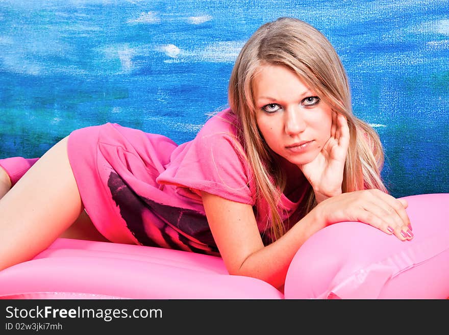 Young woman on a pink inflatable mattress posing over blue background. Young woman on a pink inflatable mattress posing over blue background