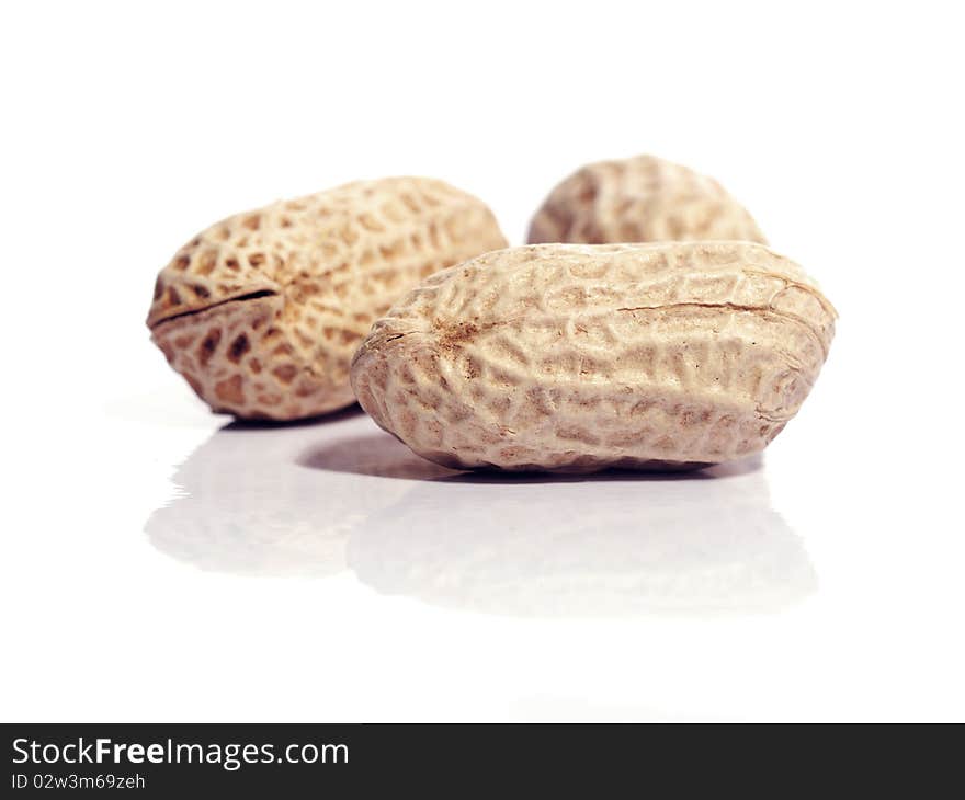 Three unshelled peanuts, isolated on white with reflection. Shallow depth of field with the nearest nut in focus.