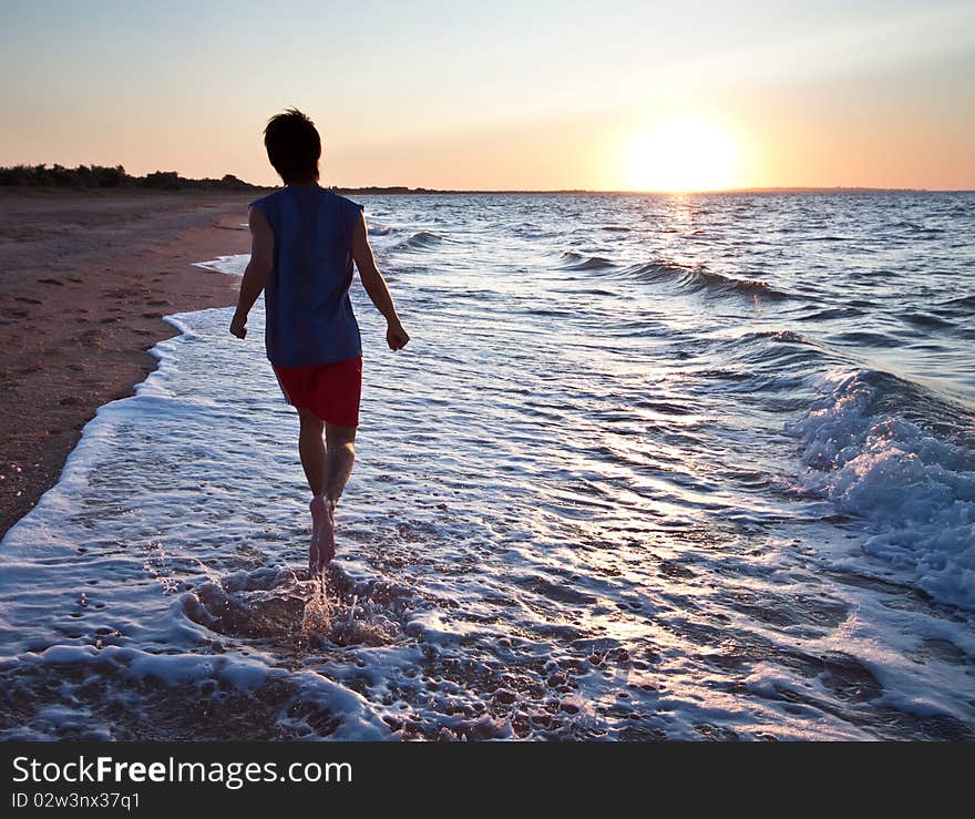 Teen boy runs at the beach on beautiful summer sunset. Teen boy runs at the beach on beautiful summer sunset