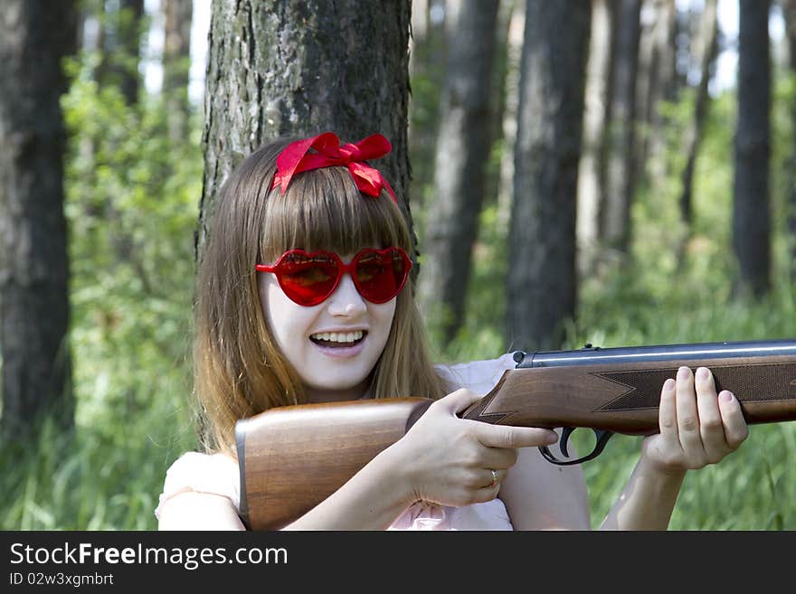 Girl with heart-shaped sunglasses holding a rifle in the forest. Girl with heart-shaped sunglasses holding a rifle in the forest