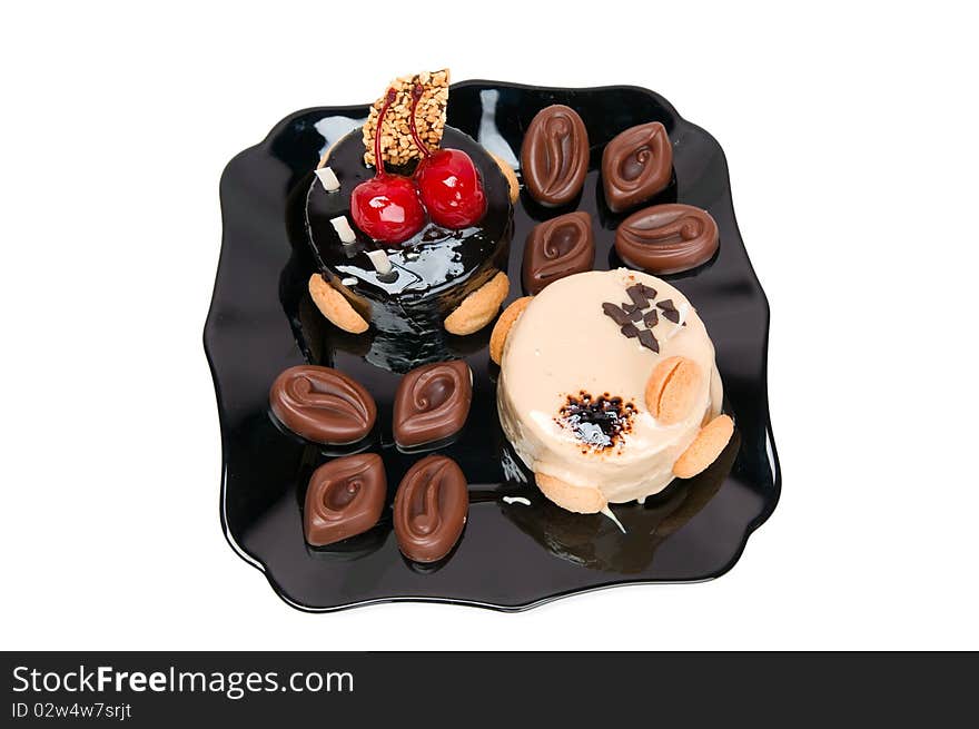 Cake with white and dark chocolate and chocolates on the black plate isolated on a white background.