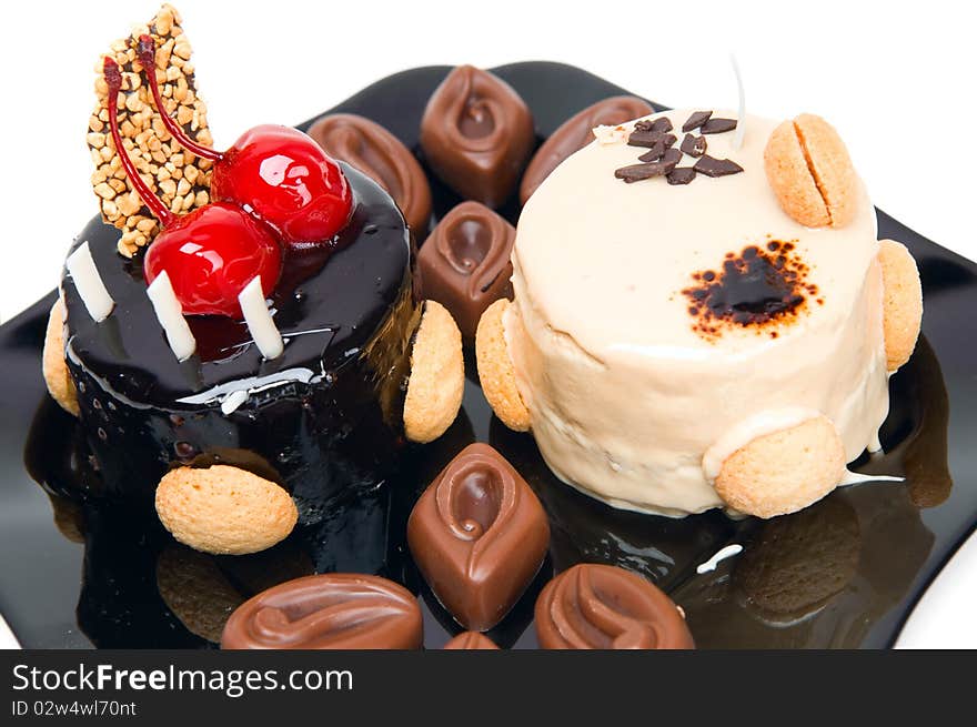 Cake with white and dark chocolate and chocolates on the black plate isolated on a white background.