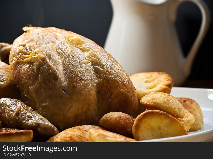 Roasted poultry with potatoes and gravy against dark background.