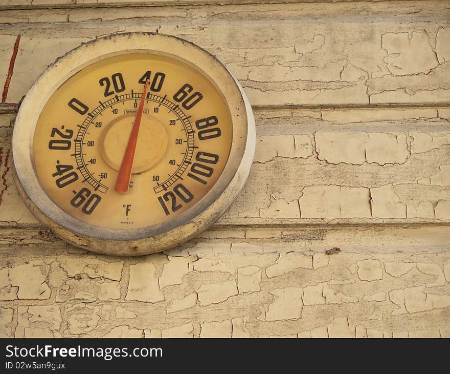 Yellow temperature gauge on a yellow wall. The gauge is old but working. The wall paint is cracked and peeling off. Yellow temperature gauge on a yellow wall. The gauge is old but working. The wall paint is cracked and peeling off.