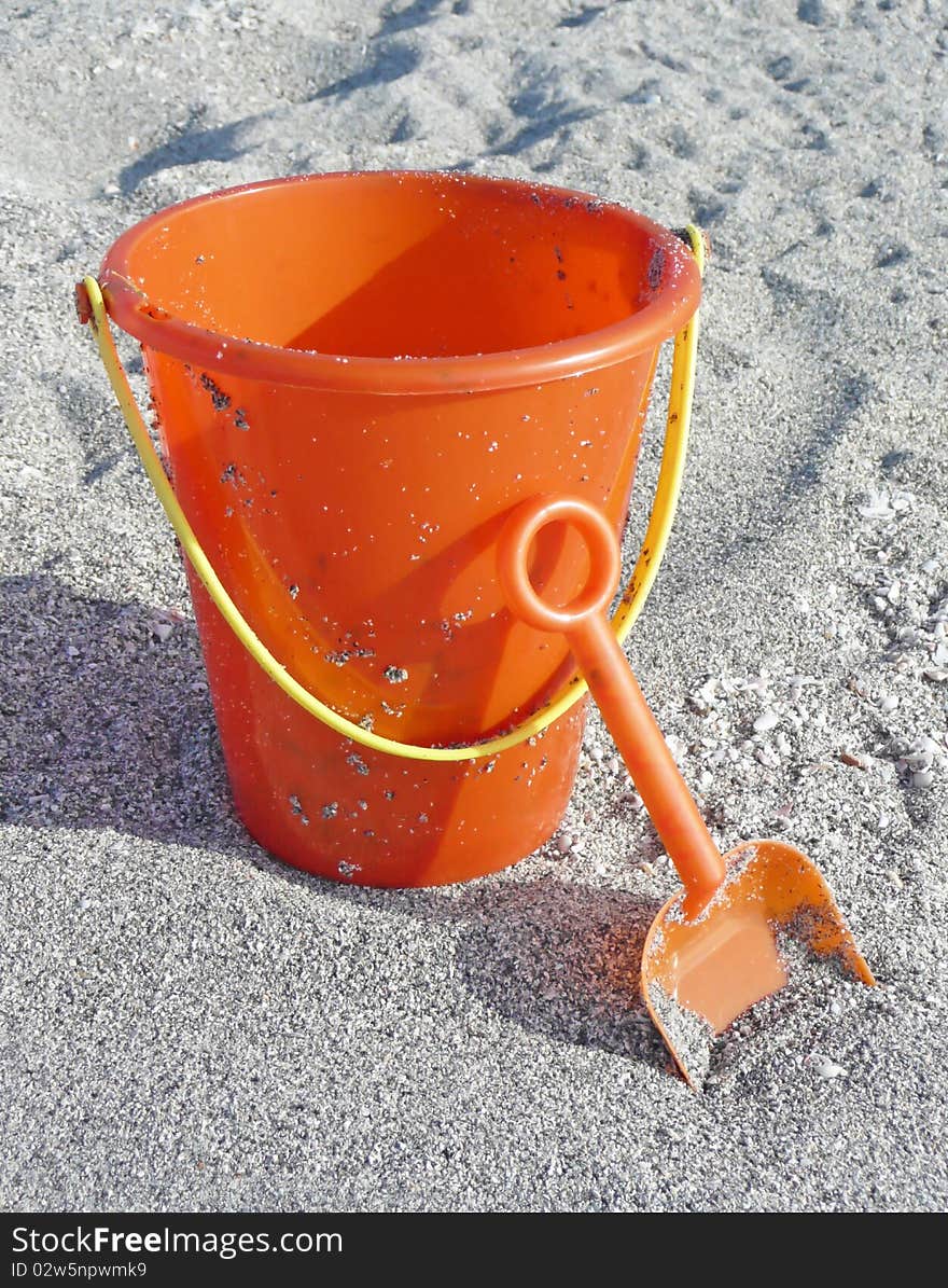 Orange bucket and shovel resting on the sandy beach