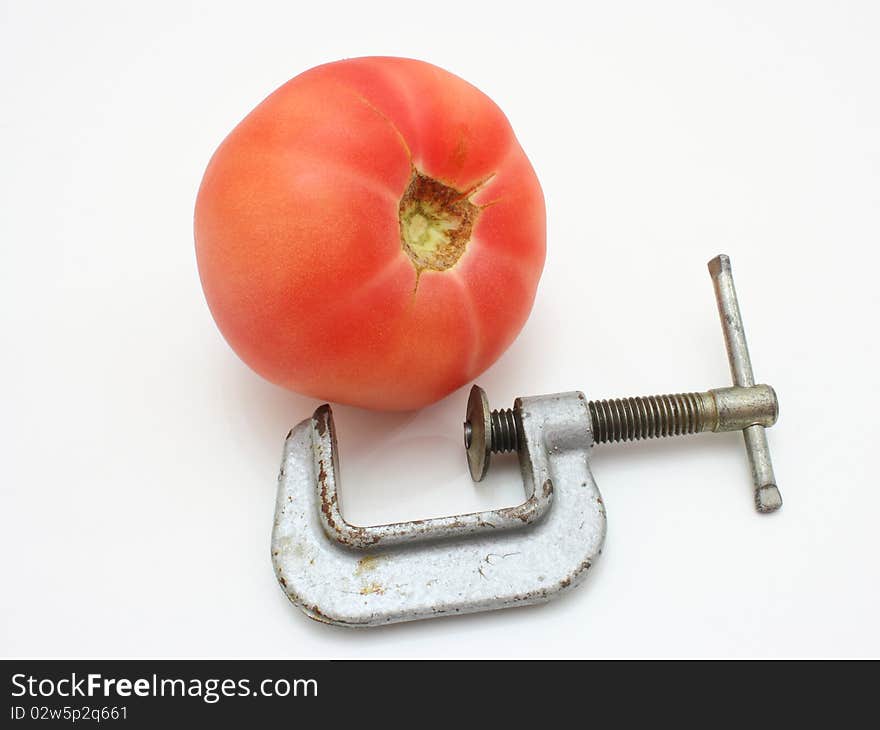 The red tomato and metal clamp lie nearby on a white background. The red tomato and metal clamp lie nearby on a white background