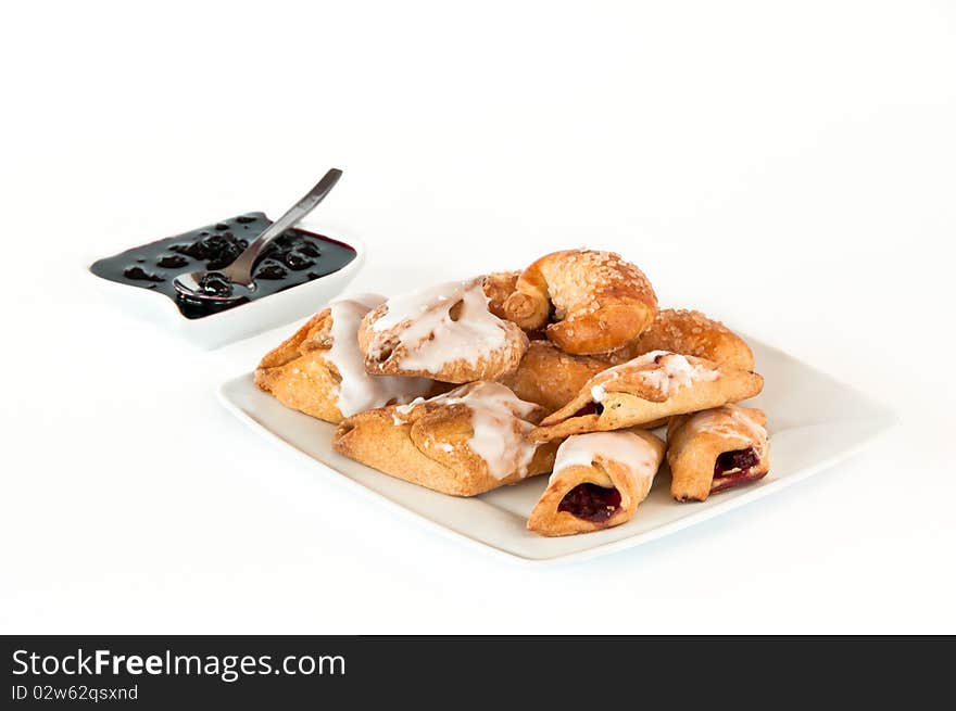 Plate of fresh, golden pastry filled with blackberry jelly and container with a spoon and jelly. Plate of fresh, golden pastry filled with blackberry jelly and container with a spoon and jelly