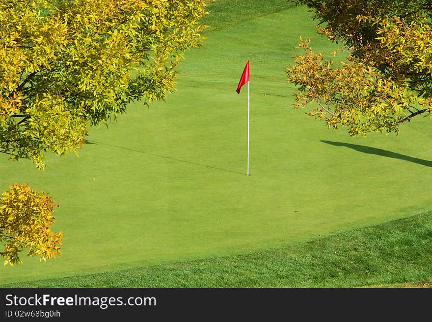 The red flag on the pin stands out on the green in the fall. The red flag on the pin stands out on the green in the fall