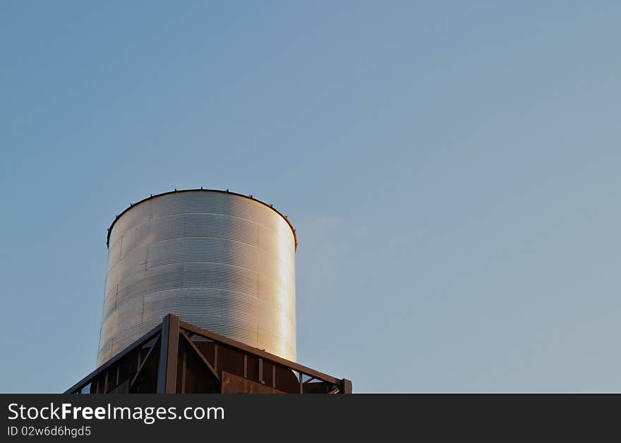 Brightly late sun lit steel water tank on tower against clear blue sky. Brightly late sun lit steel water tank on tower against clear blue sky