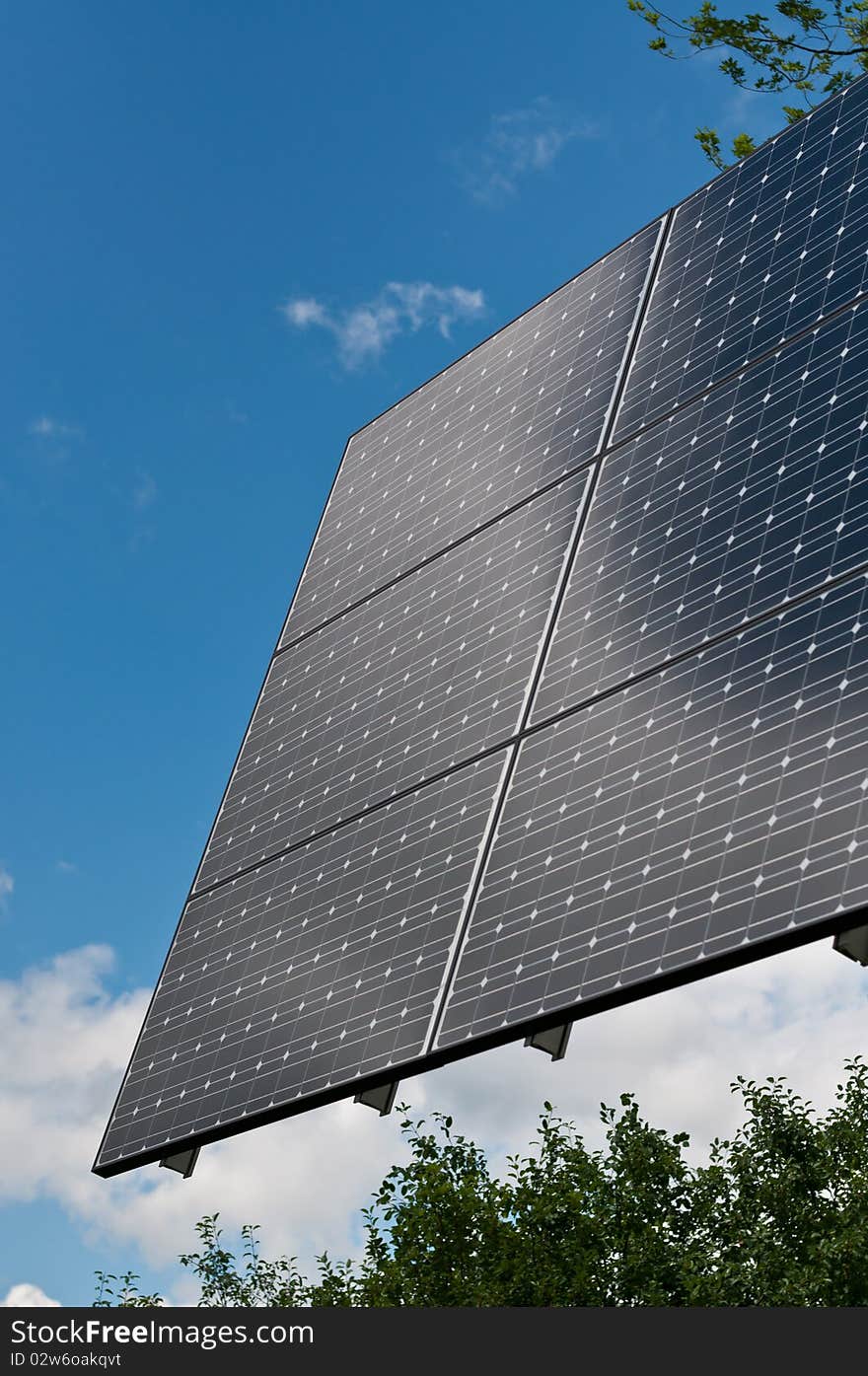 A photovoltaic solar panel array with a blue sky and green leaves in the background. A photovoltaic solar panel array with a blue sky and green leaves in the background.