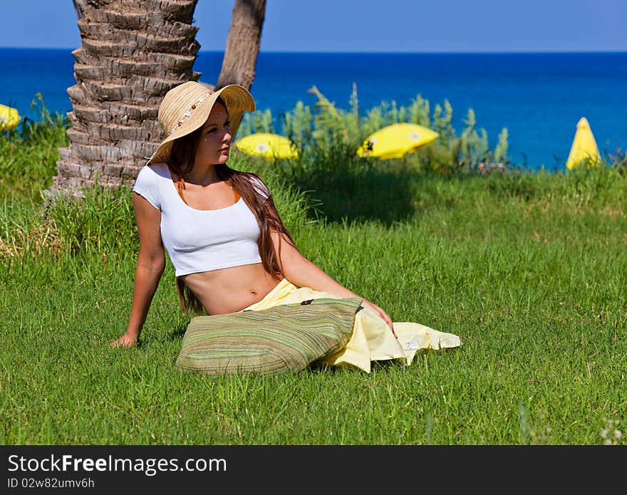 Young woman is sitting on green grass near the sea