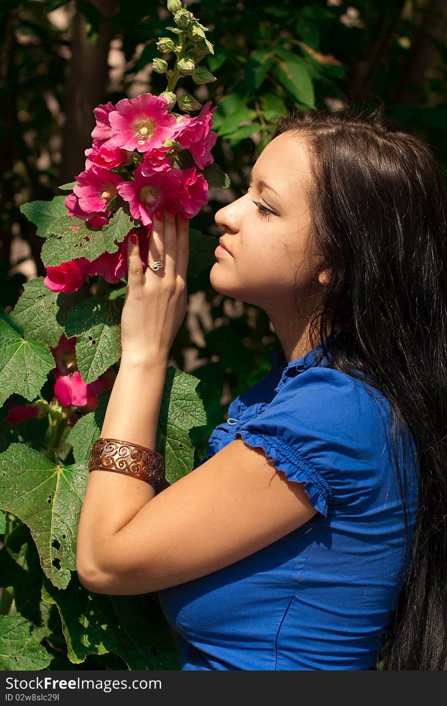 Beautiful girl with long dark hair, in blue shirt with red flower in a sunny park. Beautiful girl with long dark hair, in blue shirt with red flower in a sunny park