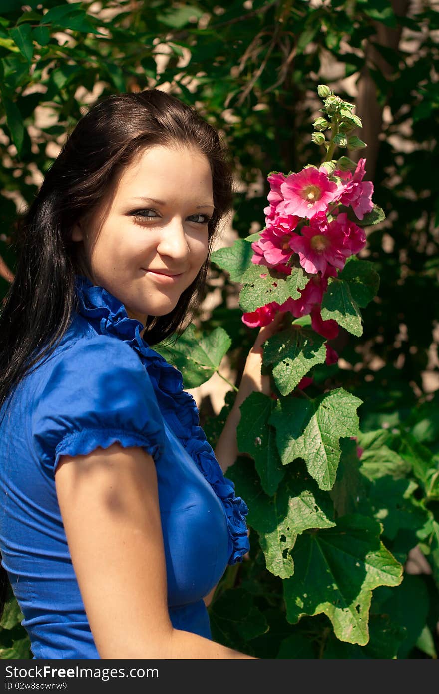 Beautiful girl with long dark hair, in blue shirt with red flower in a sunny park. Beautiful girl with long dark hair, in blue shirt with red flower in a sunny park