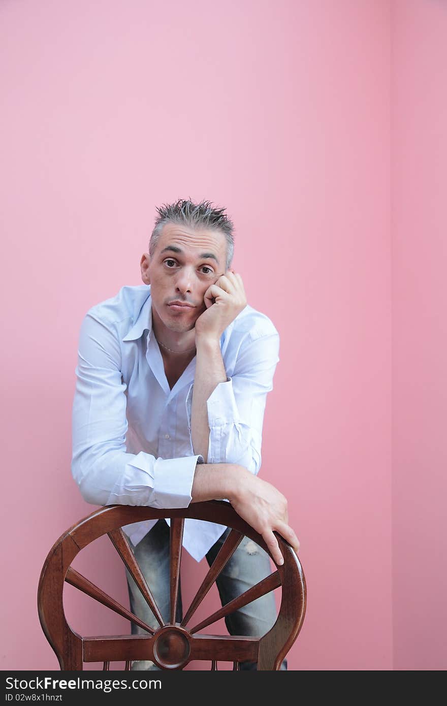 Man with blue shirt leaning on a wooden chair. Man with blue shirt leaning on a wooden chair