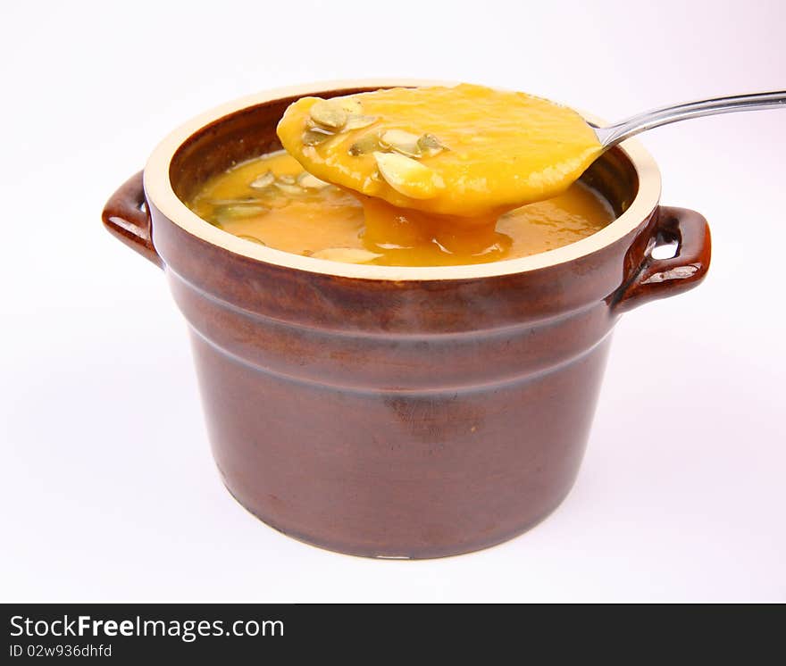 Pumpkin soup decorated with pumpkin seeds being eaten with a spoon