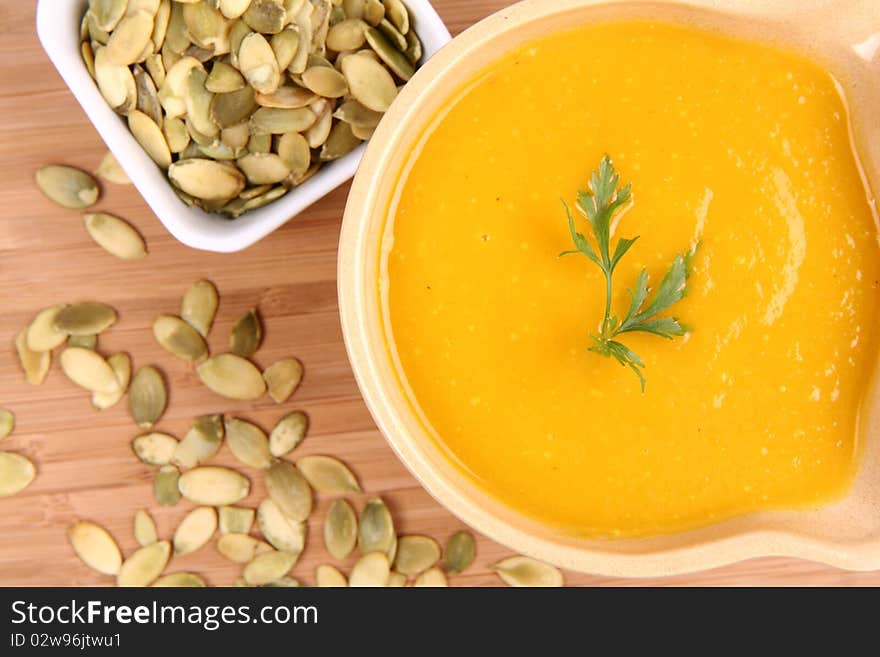 Pumpkin soup decorated with parsley and a bowl of pumpkin seeds on wooden background