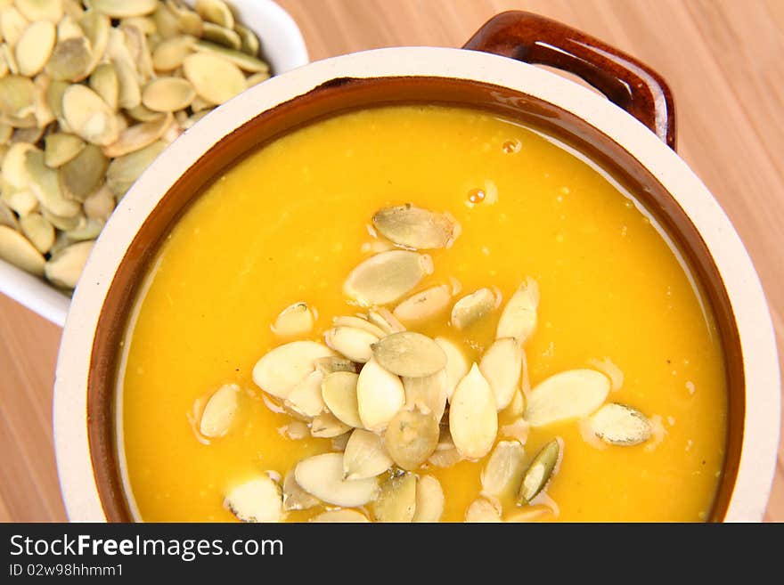 Pumpkin soup and a bowl of pumpkin seeds on wooden background