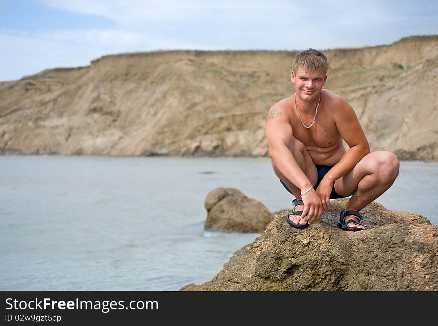 Smiling young man is squatting on the rock