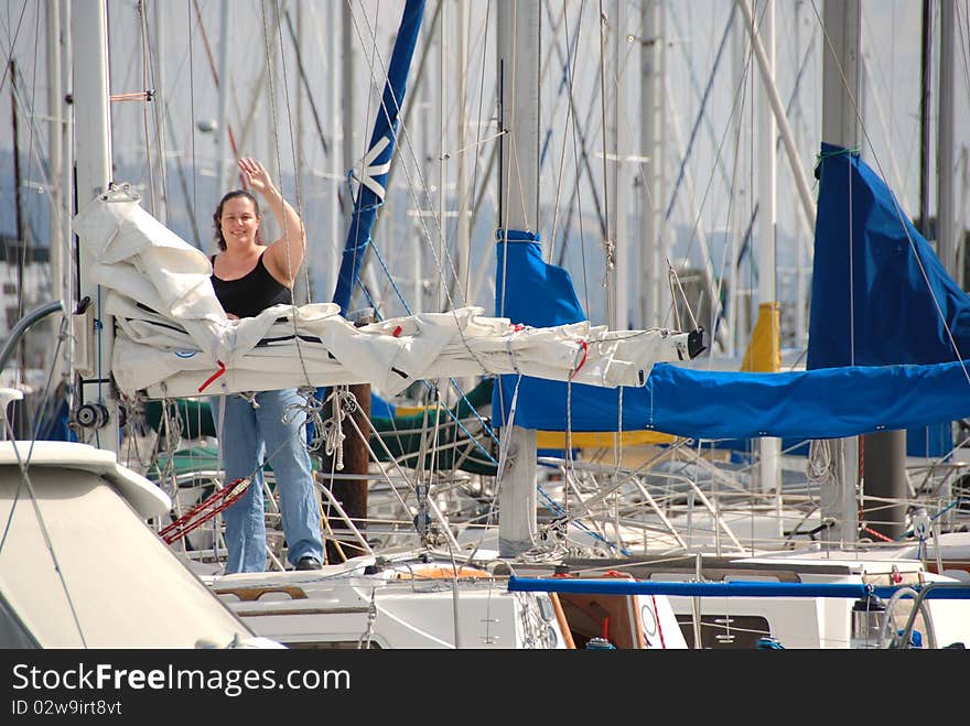 A woman stands on her sailboat near the main mast and waves to her guests to come aboard. A woman stands on her sailboat near the main mast and waves to her guests to come aboard