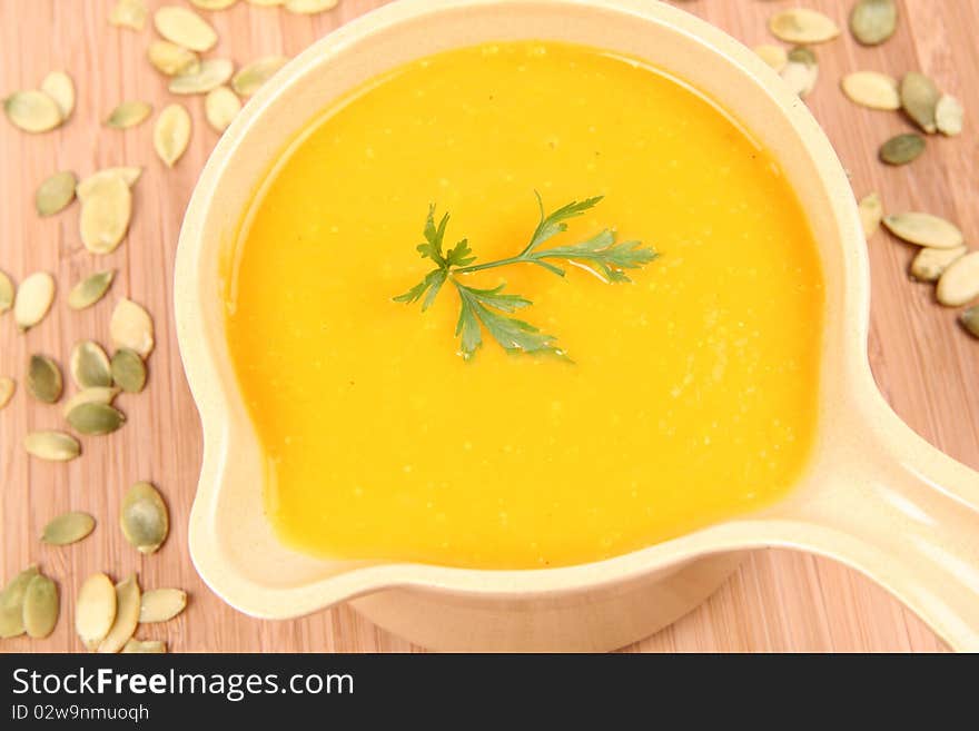 Pumpkin soup decorated with parsley and some pumpkin seeds on wooden background