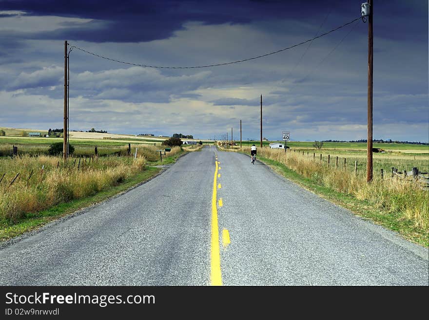 A road biker enjoys a quiet highway in Montana. Looking in the direction of a coming storm.