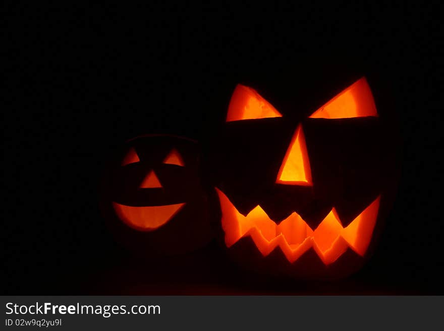 Two Jack-o'-lanterns glowing on black background with space for text