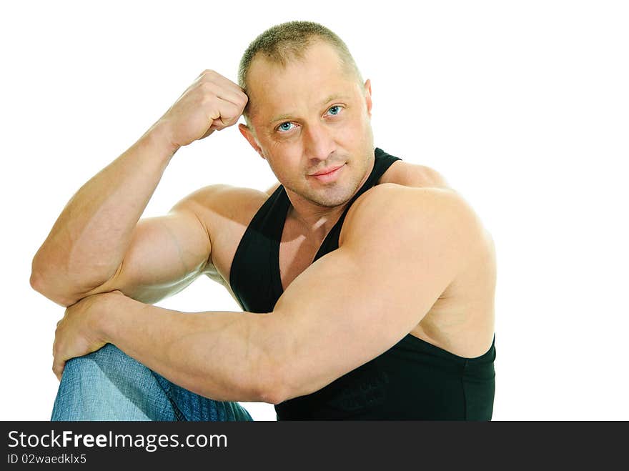 Man bodybuilder in jeans and black sleeveless sits on white background. Man bodybuilder in jeans and black sleeveless sits on white background