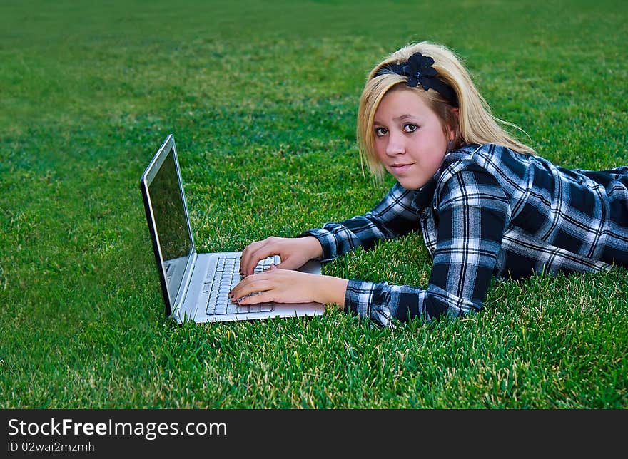 Cute teen using a laptop on a green grass. Cute teen using a laptop on a green grass.