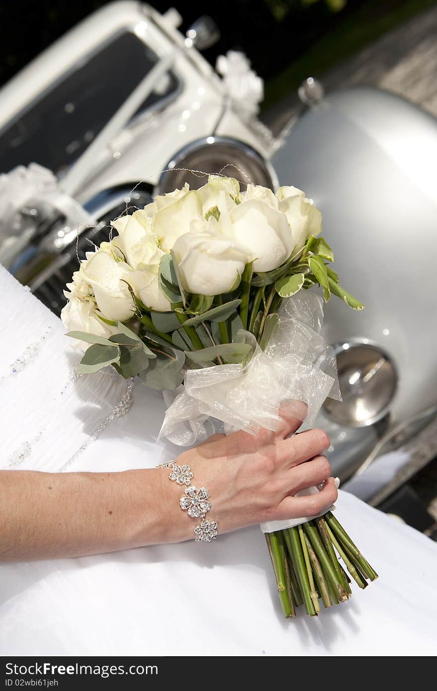 A bride's boquet of ceream roses with a vintage wedding car in the background