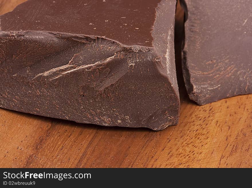 Bitter chocolate in pieces on a brown background in a plate.