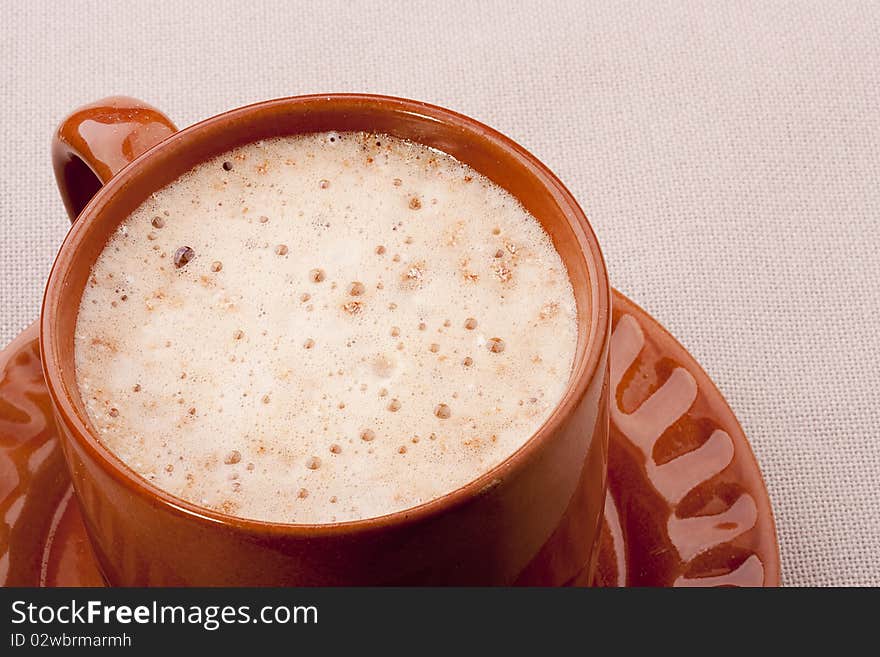 Cappuccino in a brown ceramic cup with a saucer.