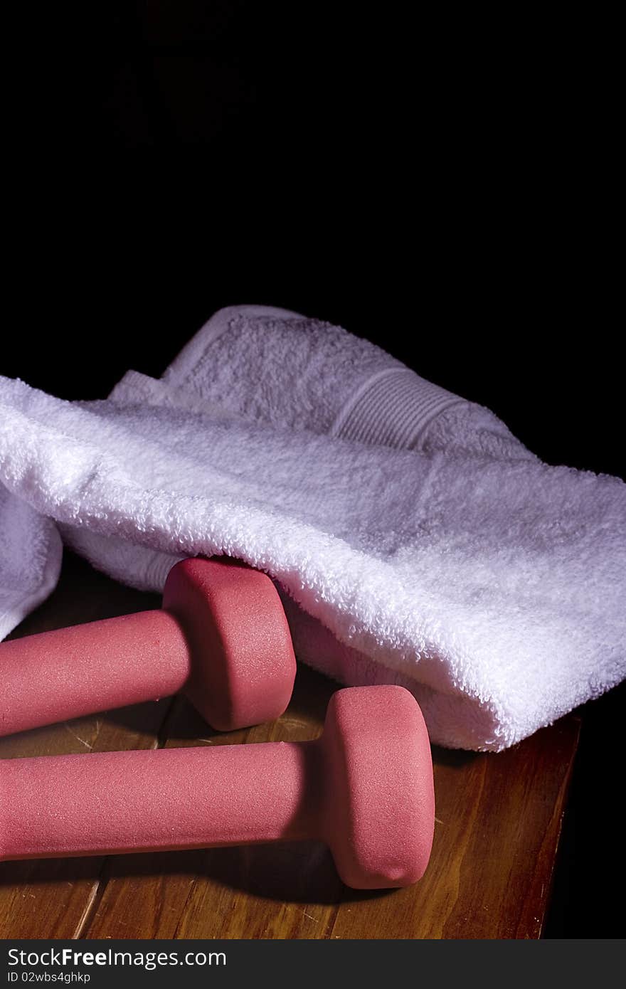 Two pink dumbbells laying next to a white towel on a wooden surface.