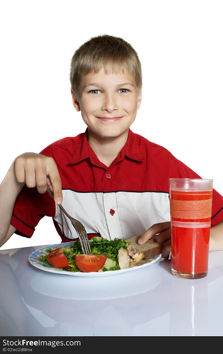 The teenager has breakfast. On a table a plate with vegetables and glass of juice.